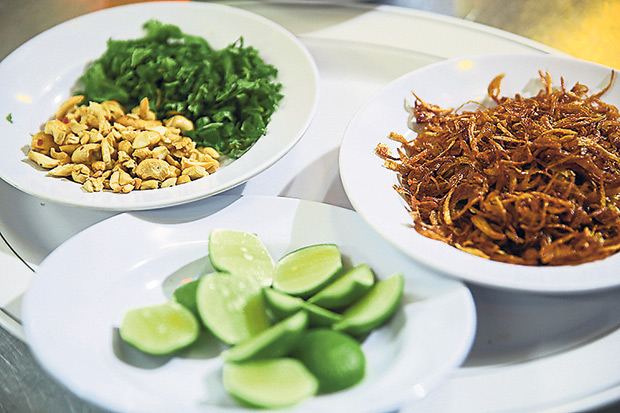 The garnishes for haleem like fried onions, toasted cashew nuts, chopped coriander and cut limes.