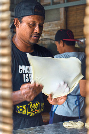 Flipping the dough for the roti canai to create more air pockets.