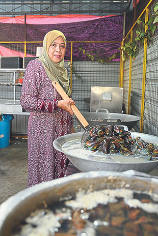 Mak Siti checking on the mussels that are being boiled in large pots in the kitchen.