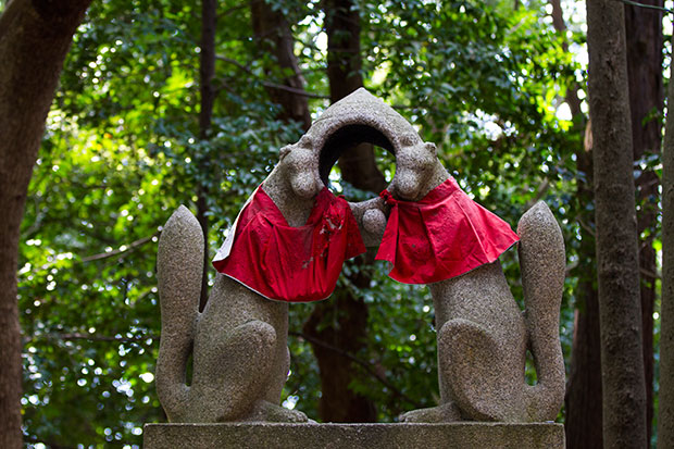 A pair of male and female kitsune statues wearing scarlet bibs (yodarekake).