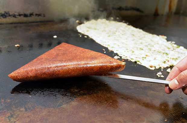 Flipping the dosa to ensure it is cooked evenly on both sides.