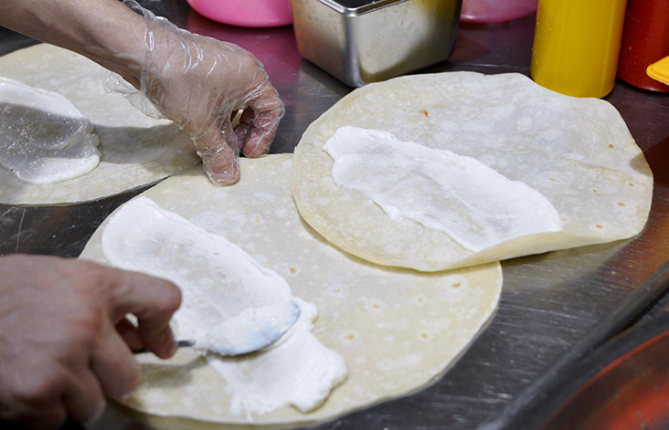 A white garlic sauce is spread first before the bread is wrapped up.