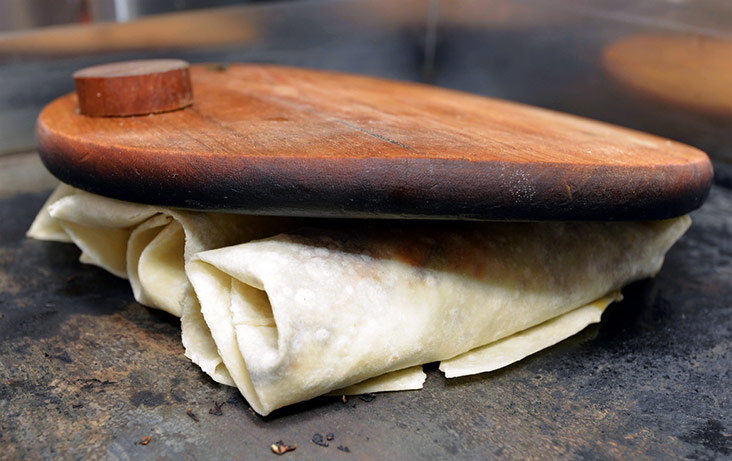 A heavy board is used to press the wraps on the hot griddle.