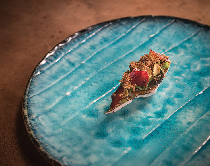 Shaped like a ‘sushi’, pop this banana heart topped with pucuk paku, pickled roses, kerdas chips and smoked daikon radish for a burst of flavours and textures.