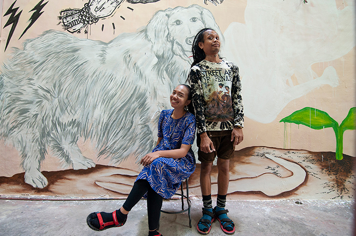 Dila and Otong, visiting artists from Indonesia, pose in front of the latter’s mural that depicts a giant dog, among other things