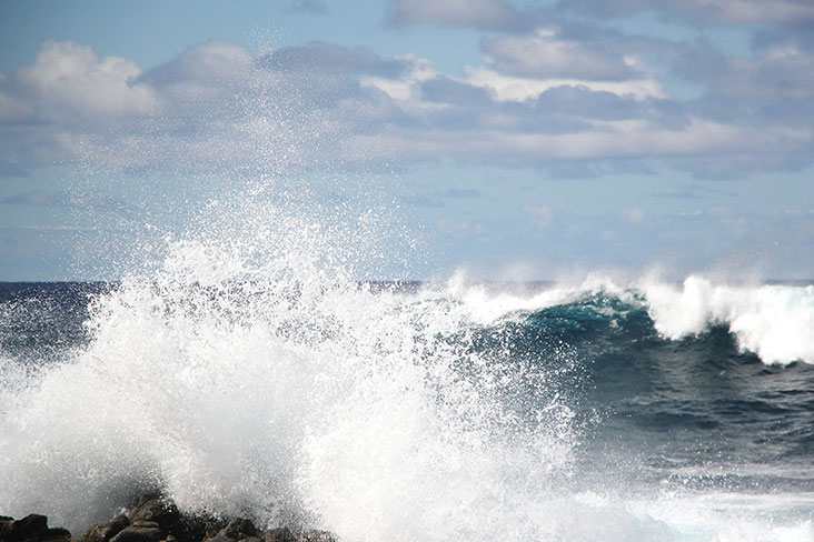 A large wave breaking on the island’s rocky coastline.