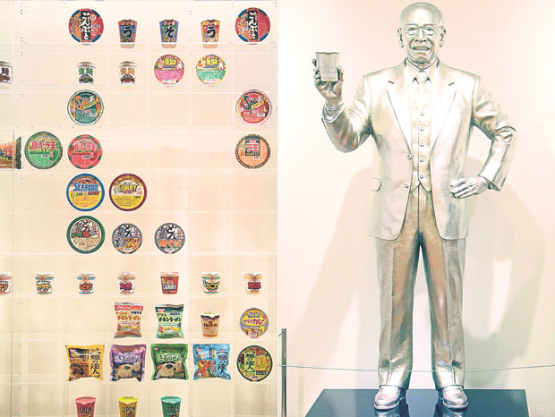 There has been over 3,000 different cup noodles product packages since the first Chicken Ramen cup noodles was released (left). A silver-hued statue of the cup noodles inventor, Momofuku Ando (right)