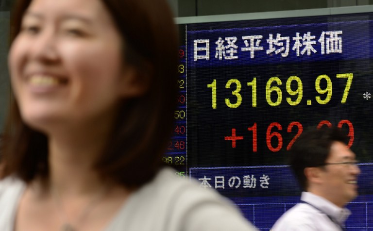 People walk past an electric quotation board flashing the Nikkei key index of the Tokyo Stock Exchange (TSE) in front of a securities company in Tokyo on June 19, 2013. 