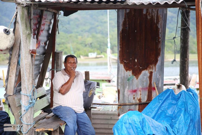 Fishermen sell fish at wooden shacks with zinc roofs beside the sea. 