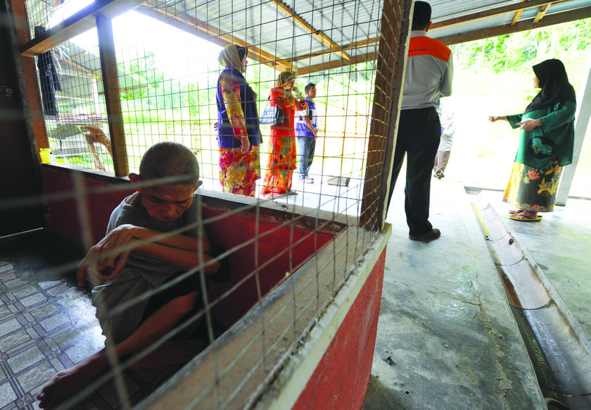 Abdul Rahman sits in his cage while Zaleha (right) speaks with welfare department officers. u00e2u20acu201d Picture by Zuraneeza Zulkifli