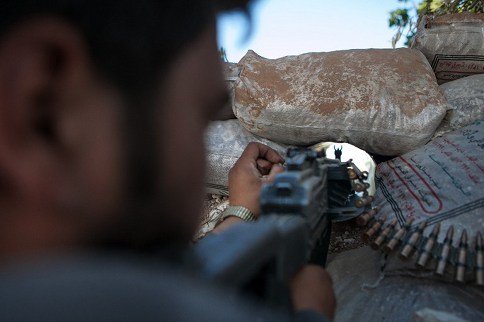 A Syrian rebel fighter points his riffle through a hole in sandbags as he holds a position in a trench, 100m far from the regime-controlled military base of Wadi Deif on June 14, 2013 in the village of Kfarruma in the Syrian province of Idlib. u00e2u20acu201d AFP pic