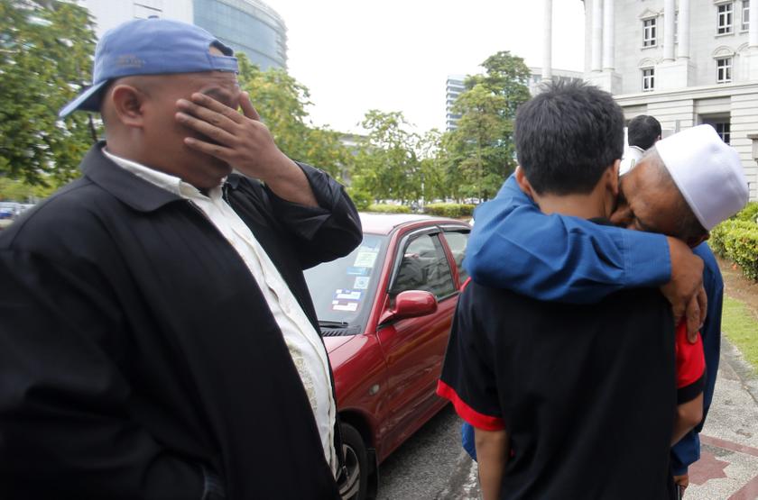 The son of Malaysia's former police special action unit personnel Sirul Azhar Umar, Shukri Azam Shirul, is hugged by family friend as Sirul's brother Khairnizam Umar wipes his tears outside the courthouse in Putrajaya  August 23, 2013. u00e2u20acu201c Reuters pic