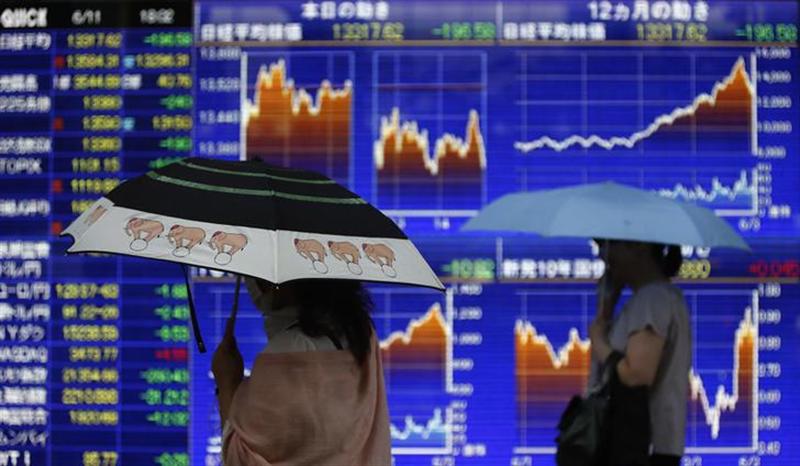 Pedestrian holding an umbrella walk past a stock quotation board displaying a graph of Japanu00e2u20acu2122s Nikkei share average and other market indices outside a brokerage in Tokyo June 11, 2013. u00e2u20acu201d Reuters pic