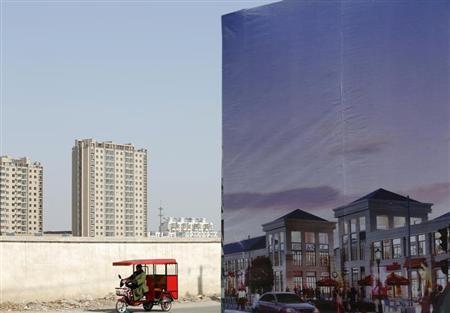 A tricycle drives past an large advertisement board of a new apartment complex at a new residential town in Beijing February 27, 2013. 