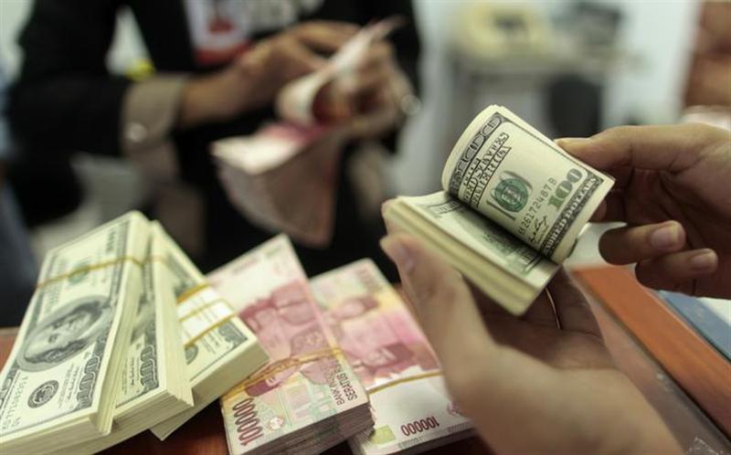 An employee of a money changer counts US dollar notes for a customer, as Indonesian rupiah is seen in the background, in Makassar January 31, 2013. u00e2u20acu201d Reuters pic