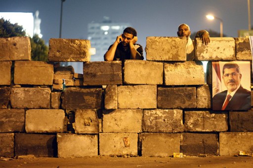 An Egyptian man talks on his phone and another looks on behind a bricks wall as Muslim brotherhood members and ousted Egyptian president Mohammed Mursi supporters rally in his support in Cairo on July 4, 2013. u00e2u20acu201d AFP pic