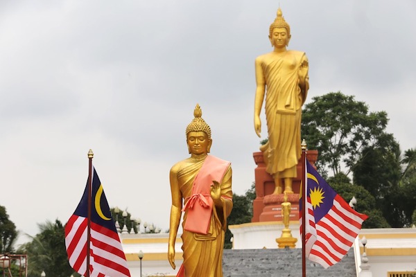 A smaller Buddha statue in Wat Pikulthong with the iconic giant Standing Buddha, or “Buddhalila”, statue in the background.