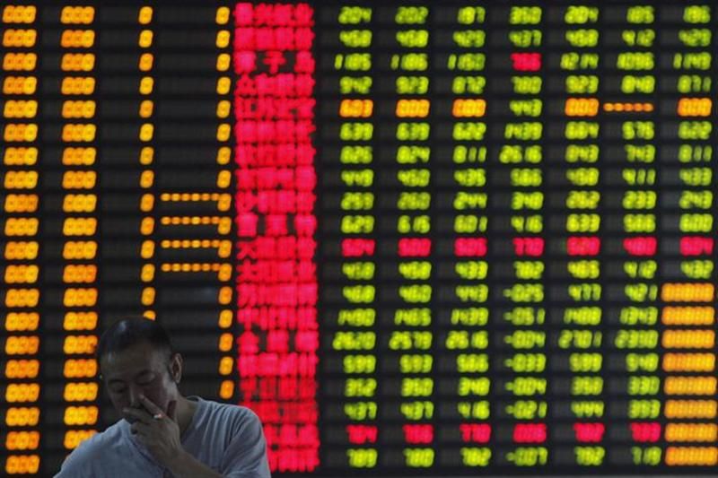 An investor smokes in front of an electronic board showing stock information at a brokerage house in Shanghai June 25, 2013