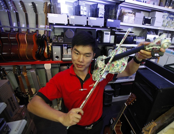 Store employee Qiu Li poses with a colourful violin that had been acquired at a Cash Converters used goods store in Singapore August 30, 2013. — Reuters pic