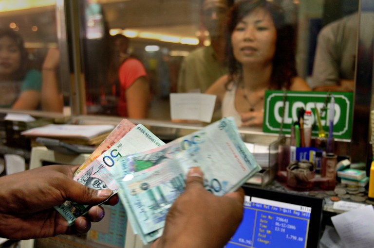 A money changer counts Malaysian ringgit bank notes while customers wait at a foreign exchange booth in downtown Kuala Lumpur. u00e2u20acu201d AFP pic