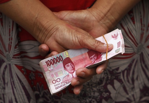 A woman holds Indonesian rupiah banknotes in front of a Bank Indonesia mobile bank in Jakarta July 15, 2013. u00e2u20acu201d Reuters pic