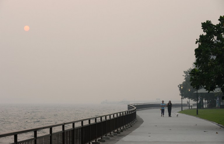 Pedestrians walk along the bay as the sun (top left) is shrouded by haze in Singapore on June 19, 2013. Indonesia plans to use weather changing technology to try to unleash torrents of rain and extinguish raging fires on Sumatra island that have cloaked n