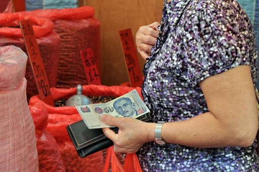 A woman holds a Singapore bank note to purchase goods at a market in Singapore on January 9, 2012. u00e2u20acu201d AFP pic