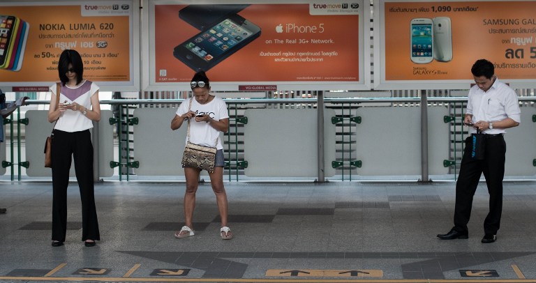 This picture taken on March 20, 2013 shows people looking at their smartphones while waiting for a train at a BTS station in Bangkok. u00e2u20acu201d AFP pic