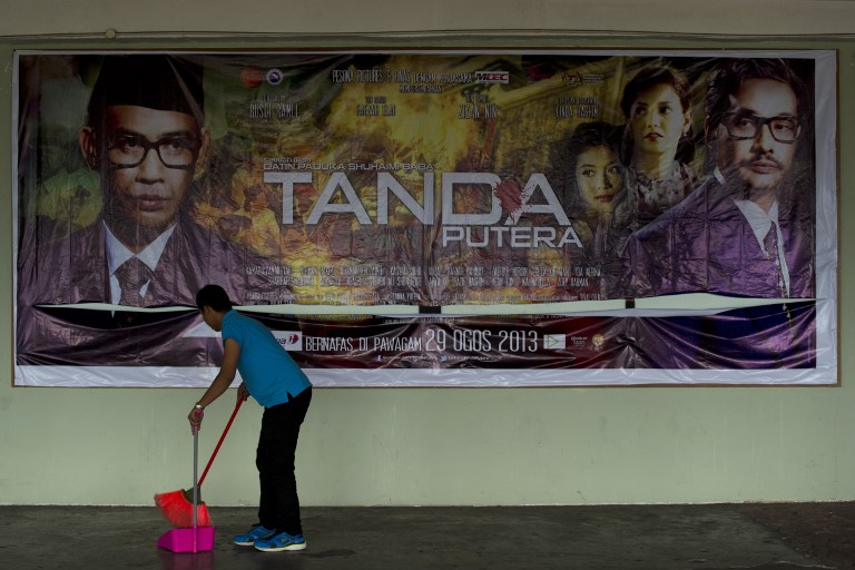 This picture taken on August 27, 2013 shows a worker cleaning the floor in front of a poster advertising movie named 'Tanda Putera' at a local cinema in Kuala Lumpur. u00e2u20acu201c AFP pic