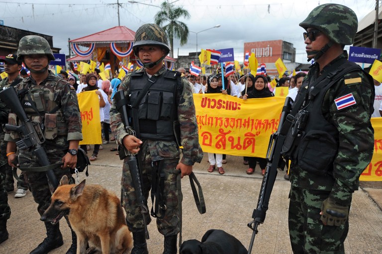 Thai security stand watch as Muslim villagers (background) hold national flags and banners during an anti-violence rally in southern Thailand's Narathiwat province on December 22, 2012. u00e2u20acu201c Reuters pic