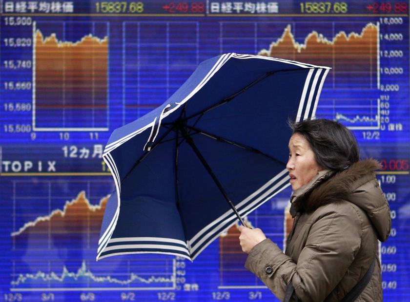 File photo shows a pedestrian holding an umbrella walking past an electronic board displaying graphs of the recent movement of Japanu00e2u20acu2122s Nikkei average outside a brokerage in Tokyo December 19, 2013. u00e2u20acu201d Reuters pic