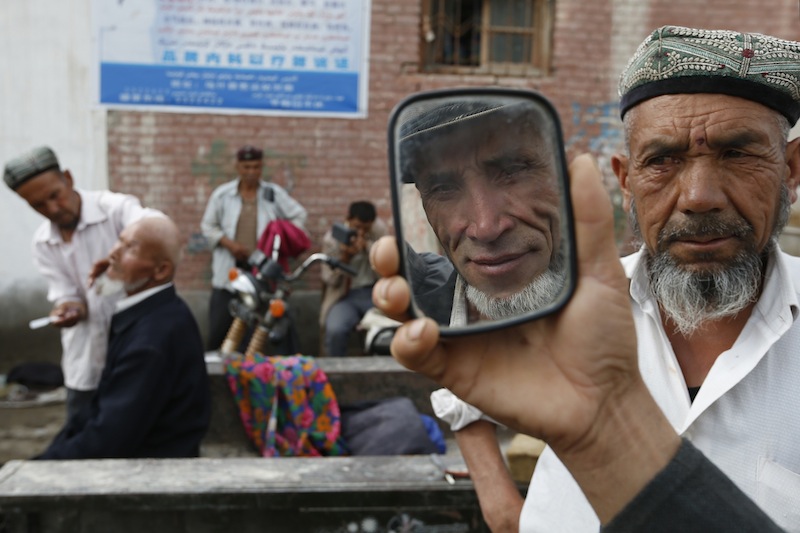 An ethnic Uighur man checks a mirror after getting his beard shaved by a barber (right) on a street in Aksu, Xinjiang Uighur Autonomous Region July 21, 2013. u00e2u20acu201d Reuters pic